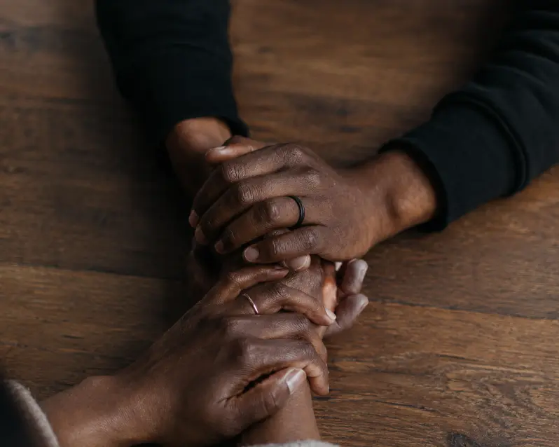 Two people holding hands across a table in support